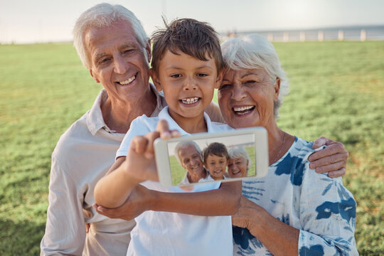 Phone, selfie and happy grandparents with child outdoor in nature on family picnic together. Happiness, smile and elderly man and woman in retirement taking picture on smartphone with boy grandchild.