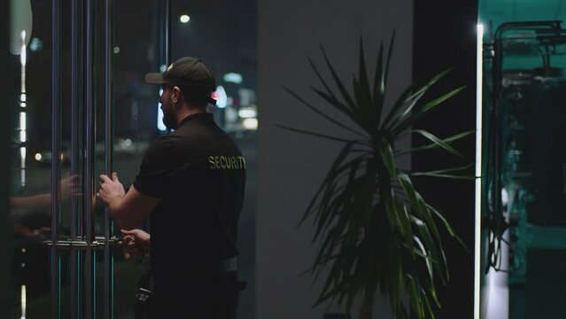 Guard or security worker walking , closing door and turning  plate with open closed sign at night . Guard dressed security uniform working inside storage or shop . Concept of night shift work