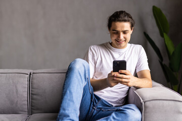 Attractive young man sitting on a floor in the living room, using mobile phone