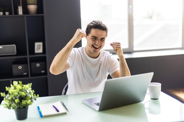 Happy man celebrate great news opportunity got read by e-mail. Excited man sit in kitchen look at laptop screen with clenched fists feels incredible amazed received good notice. Sale, discount concept
