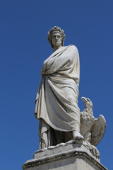 White marble statue of Italian poet Dante Alighieri, by sculptor Enrico Pazzi, in Piazza Santa Croce, Florence, Italy. Literature concept. Vertical full length shot with blue sky on background.