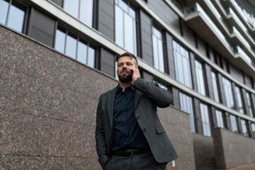 portrait of an adult male entrepreneur with a mobile phone against the backdrop of an office building, business economic consultant concept