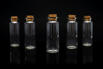 Five empty glass bottles on a black background with corks. Transparent glass vessels for various liquids. Set of identical closed test tubes on a black background