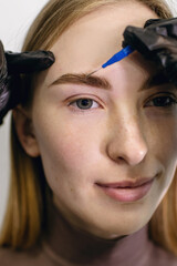 Eyebrow master using a micro brush shapes combing the eyebrows of a red-haired girl with freckles...