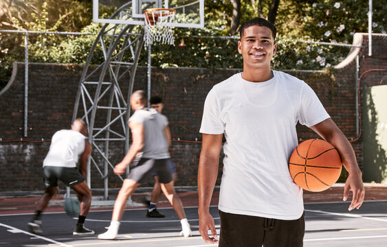 Portrait of african man, basketball and athlete on basketball court outdoors. Basketball player, fitness and healthy sports training on court in urban city with teammates playing in background - Powered by Adobe