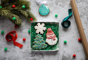 Gingerbreads in the form of snowman, Christmas tree and snowflake in gift box next to pine branch, ribbons and wrapping paper. Christmas and New Year background. Preparing of Christmas gifts. 