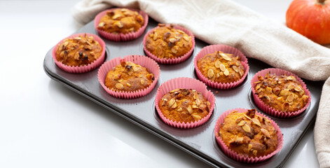Homemade pumpkin muffins with pumpkin seeds and walnut pieces. Fall baking for Thanksgiving and Halloween. Cupcakes in baking dish on linen napkin. Selective focus. Close up. Copy space