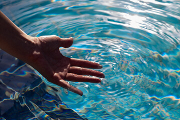 Man's hand inclear transparent water of pool.