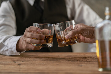 
Close-up of serious businessman holding whiskey glass shows concept of executive privilege. Soft focus. Close-up view of two men in formal wear whiskey clashing glasses.
