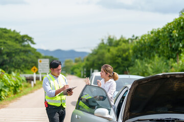 An insurance agent talking to a woman outside on the road after a car accident.