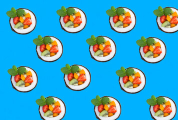 Fruit salad in the half coconut on the blue background. Flat lay. Pattern.
