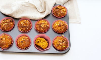 Fototapeta na wymiar Homemade pumpkin muffins with pumpkin seeds and walnut pieces. Autumn baking for Thanksgiving and Halloween. Cupcakes in baking dish and linen napkin. Selective focus. Top view. Close-up. Copy space