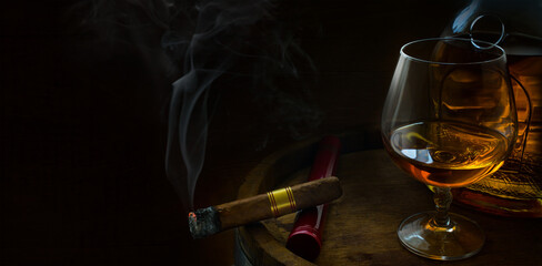 a glass of a luxurious alcoholic drink, an oak barrel, a bottle of cognac and a cigar on a dark background; men's club banner with copy space