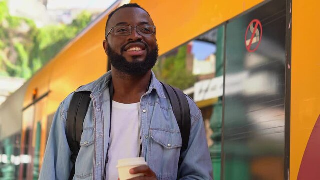 Low-angle view of a Young African man with coffee at a European terminal train station. Tourist travel by train on vacation time holiday weekend trip.