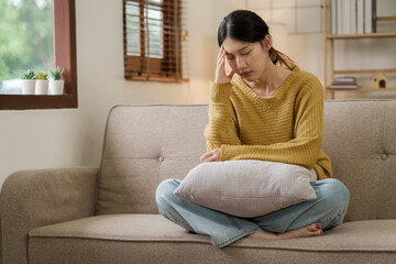 Obraz premium Asian woman with a headache and stress while sitting on the sofa at home