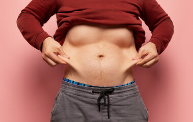 Naklejka premium Closeup male hands stretching skin on his belly, man showing to camera his abdomen. Concept of dieting, sport, fitness, healthy lifestyle, body positive and wellbeing