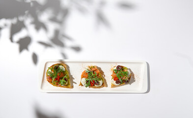 Aesthetic composition with salmon bruschetta on white background with shadows from flowers. Italian bruschetta with salmon, avocado, cheese and olives on fine dining in summer. Elegant menu concept.