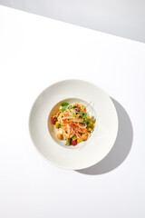Elegant food - salad with shrimp and avocado on white table with harsh shadow. Flashy food concept. Seafood salad with shrimp, tomatoes and avocado on white plate with sunlight.