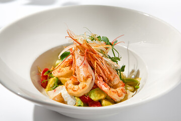 Elegant food - salad with shrimp and avocado on white table with harsh shadow. Flashy food concept. Seafood salad with shrimp, tomatoes and avocado on white plate with sunlight.