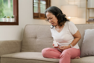 Mature Woman Suffering Stomach Ache at home and touching her lower stomach while suffering from...