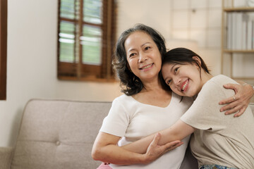 Elderly mother and grown daughter holding hands sitting on the sofa hugging.