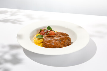 Traditional italian dish - osso buco with risotto milanese. Stew meat on bone with rice on white plate. Summer italian dining. Italian osso buco with garnish with hard shadows