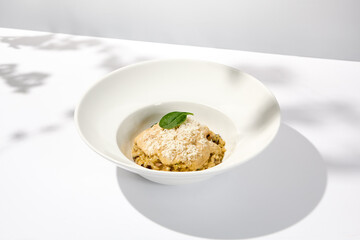 Italian food - mushrooms risotto with creamy espuma on light background. Mushroom risotto with cheese in summer menu Italian risotto with hard shadows from tree leaves. Trendy menu concept