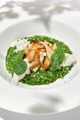 Green risotto with squid and stracciatella cheese on white plate. Creamy risotto with spinach, calamari and creamy cheese. Italian risotto with squid on light background with shadows of leaves