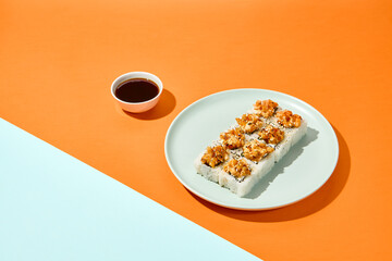 Baked maki sushi in ceramic plate on coloured background. Sushi roll with shrimp tartare in trendy style on orange and blue colour backdrop Maki roll with hard shadows in minimal style
