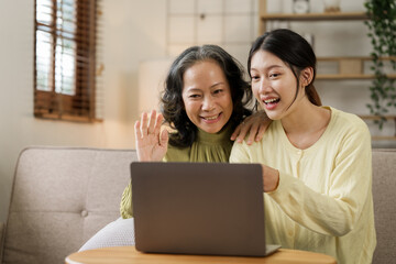 Asian mature mom with daughter using laptop while sitting on sofa, mother day concept.