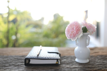 pink roses in a white vase and leather notebook on wooden table