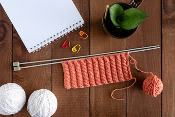 Knitting on spokes with a pattern. Flat lay with yarn, knitting needles, notepad on a wooden table. Hobby concept.