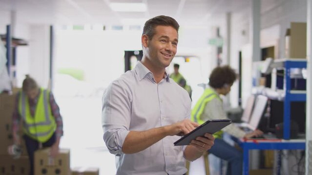 Male Manager In Busy Logistics Distribution Warehouse Using Digital Tablet