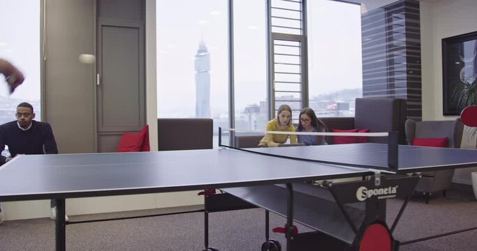 Startup business everyday life. Businesspeople playing ping pong tennis at modern creative office space while group of female coworkers working on project and have meeting in background.