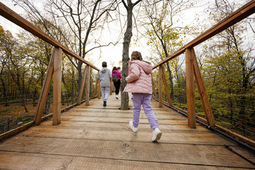 Children with mother walking at wooden bridge in autumn forest.