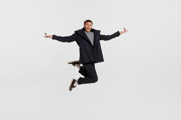Portrait of young boy, sailor in striped shirt and jacket posing, jumping isolated over white background