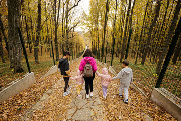 Fototapeta premium Back of mother with four kids on path at autumn fall forest.