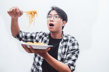 Portrait of Happy Asian man in casual shirt eats instant noodles using fork hungrily isolated over...