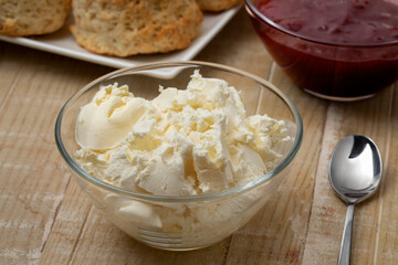 Glass bowl with clotted cream in front of scones and jam close up   