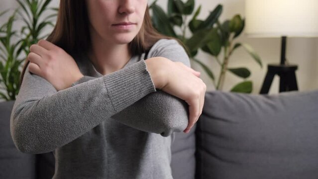 Young woman having pain in his elbow, warming up injured hand after trauma. Sad female sitting on sofa massage painful hand. Unhealthy girl holding her elbow suffering from elbow pain. Selective focus