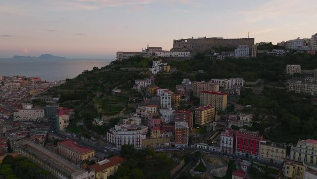 Aerial slide and pan footage of medieval castle on hill and apartments buildings in slope bellow. Castel SantElmo at dusk. Naples, Italy