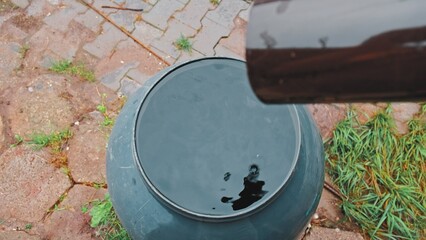 Fototapeta na wymiar Drops of Water Dripping from Plastic Gutter into Overflowing Plastic Barrel Reservoir for Collecting Rainwater