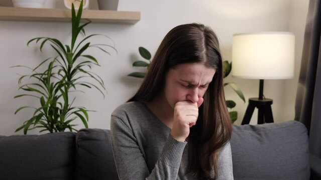 Close up of unhealthy young woman coughing sit on couch, suffering from bronchitis disease or painful uncomfortable feelings in throat, caught cold, first flu grippe covid19 symptoms, immunity concept