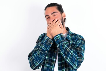 Fototapeta premium Upset young bearded hispanic man wearing plaid shirt over white background , covering her mouth with both palms to prevent screaming sound, after seeing or hearing something bad.