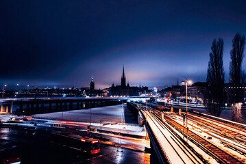 Illuminated railroad track and highway with silhouette church in background during winter