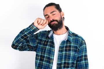 Unhappy young bearded hispanic man wearing plaid shirt over white background  crying while posing at camera whipping tears with hand.