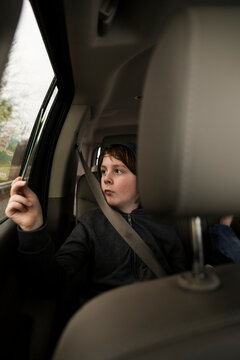 Serious Boy Looking At Comic Book By Window While Traveling In Car