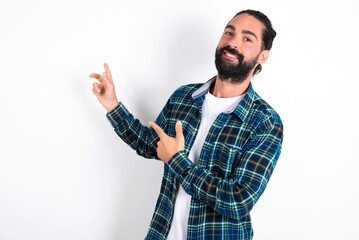 Fototapeta premium young bearded hispanic man wearing plaid shirt over white background with positive expression, indicates with fore finger at blank copy space for your promotional text or advertisement.