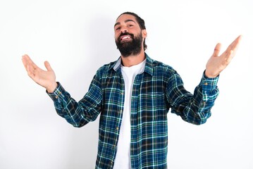 Naklejka premium Cheerful young bearded hispanic man wearing plaid shirt over white background making a welcome gesture raising arms over head.