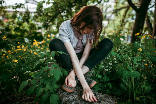 A Woman Is Sitting On A Stone In The Middle Of Flowers